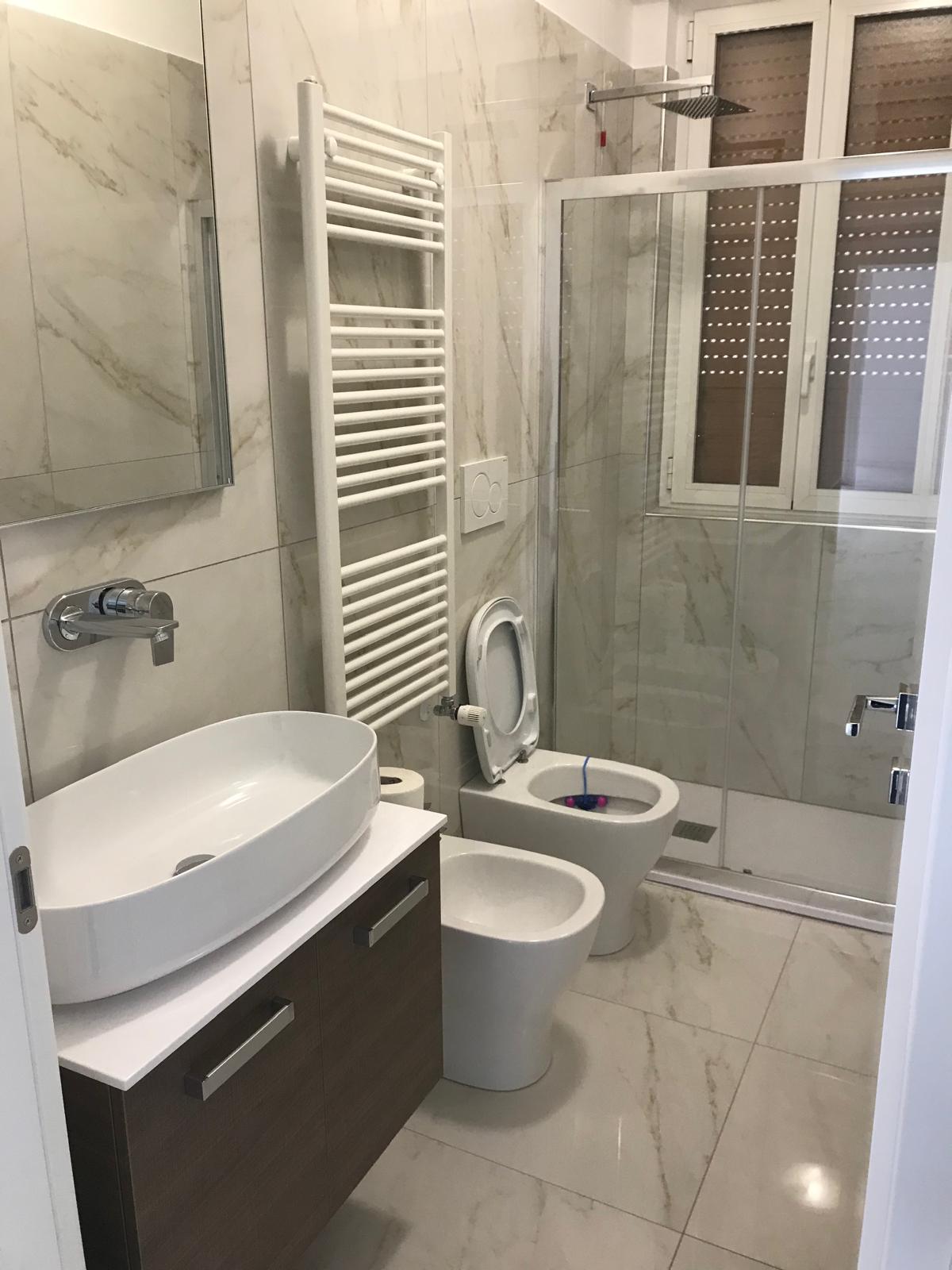 Bagno chiaro con doccia in vetro e piastrelle effetto marmo