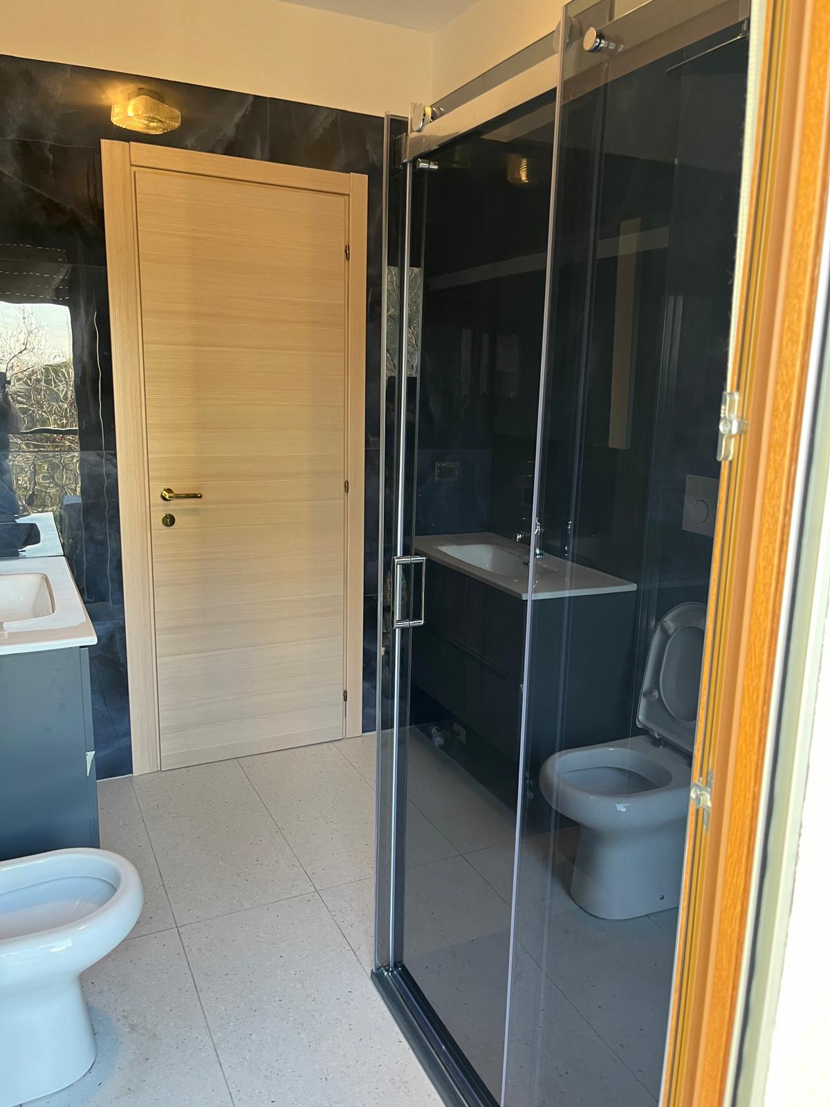 Bagno con piastrelle effetto marmo nero e box doccia in vetro fumé