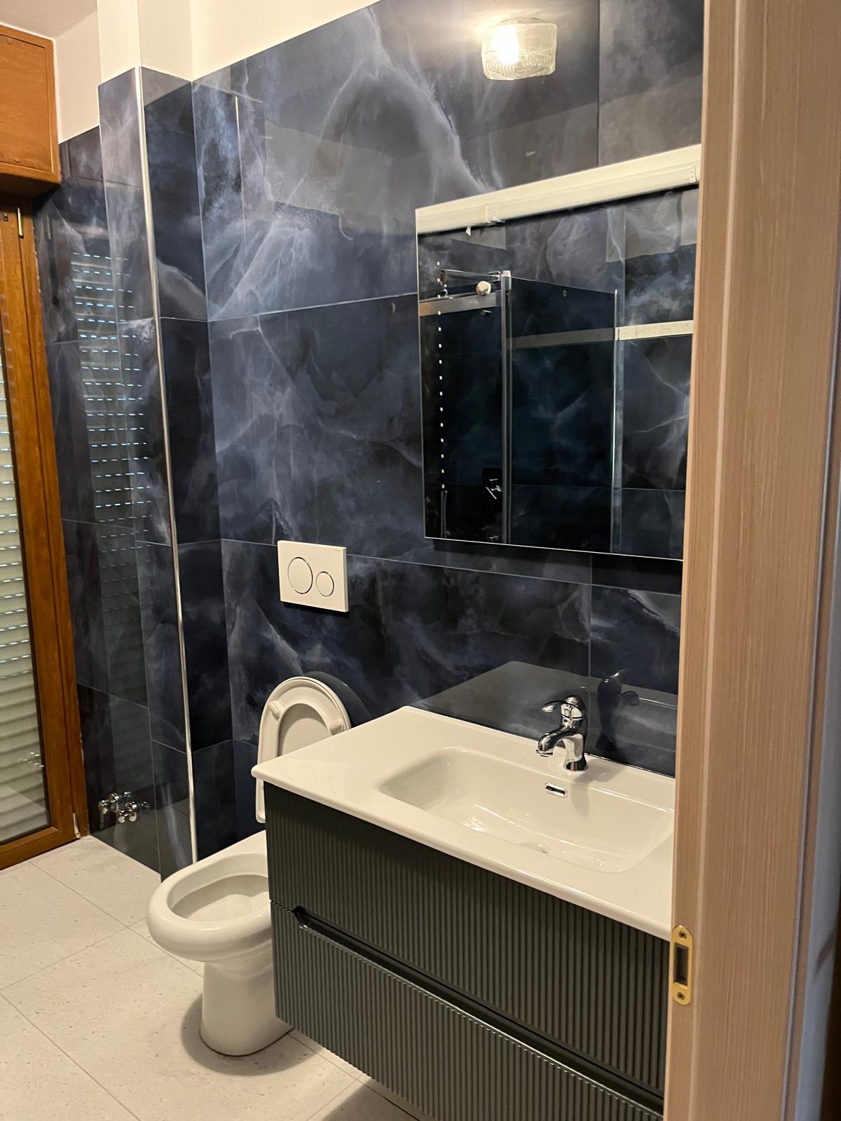 Bagno scuro con mobile sospeso e piastrelle effetto marmo blu